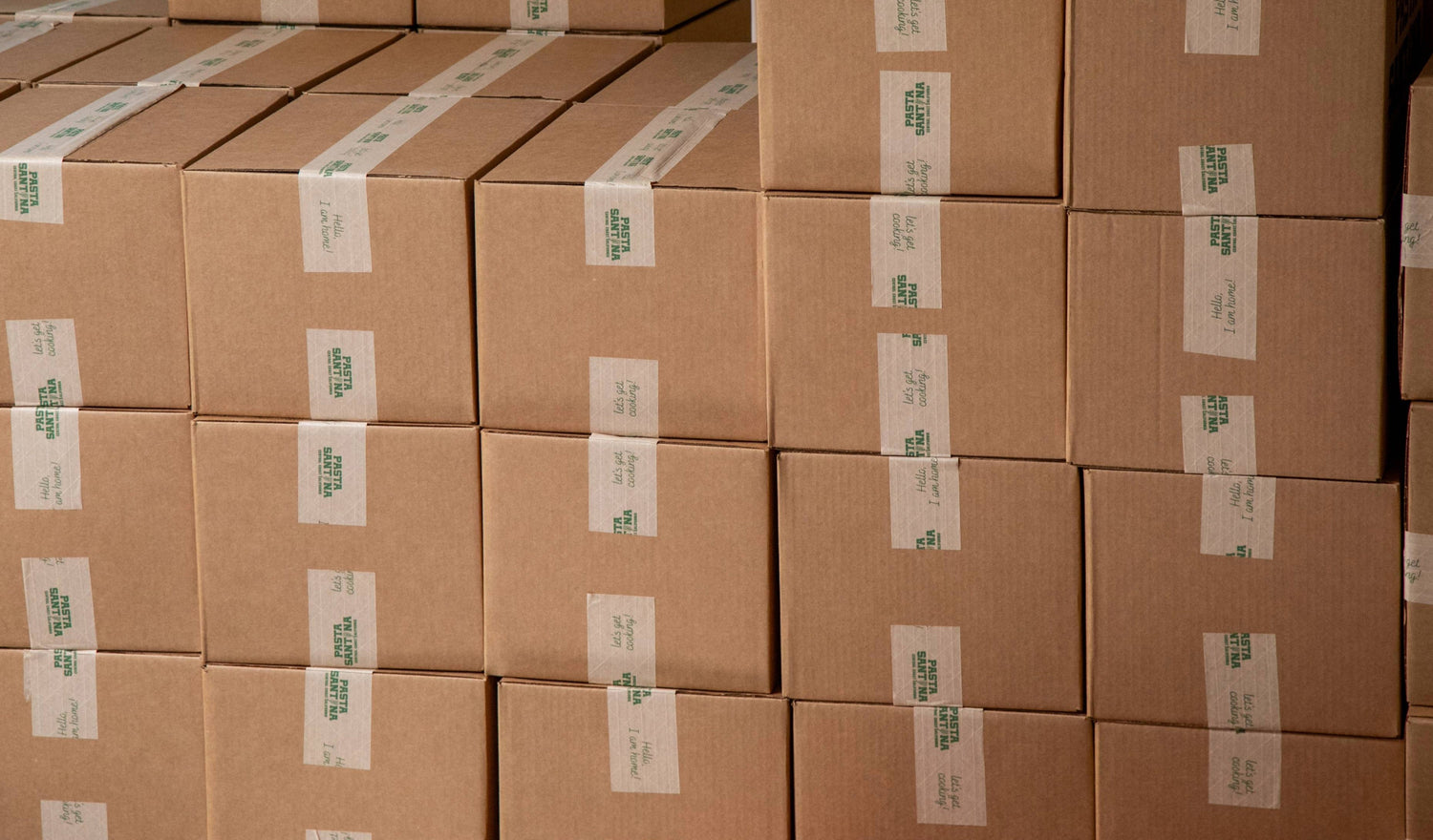 Stack of brown cardboard boxes with green and white labels in a warehouse setting