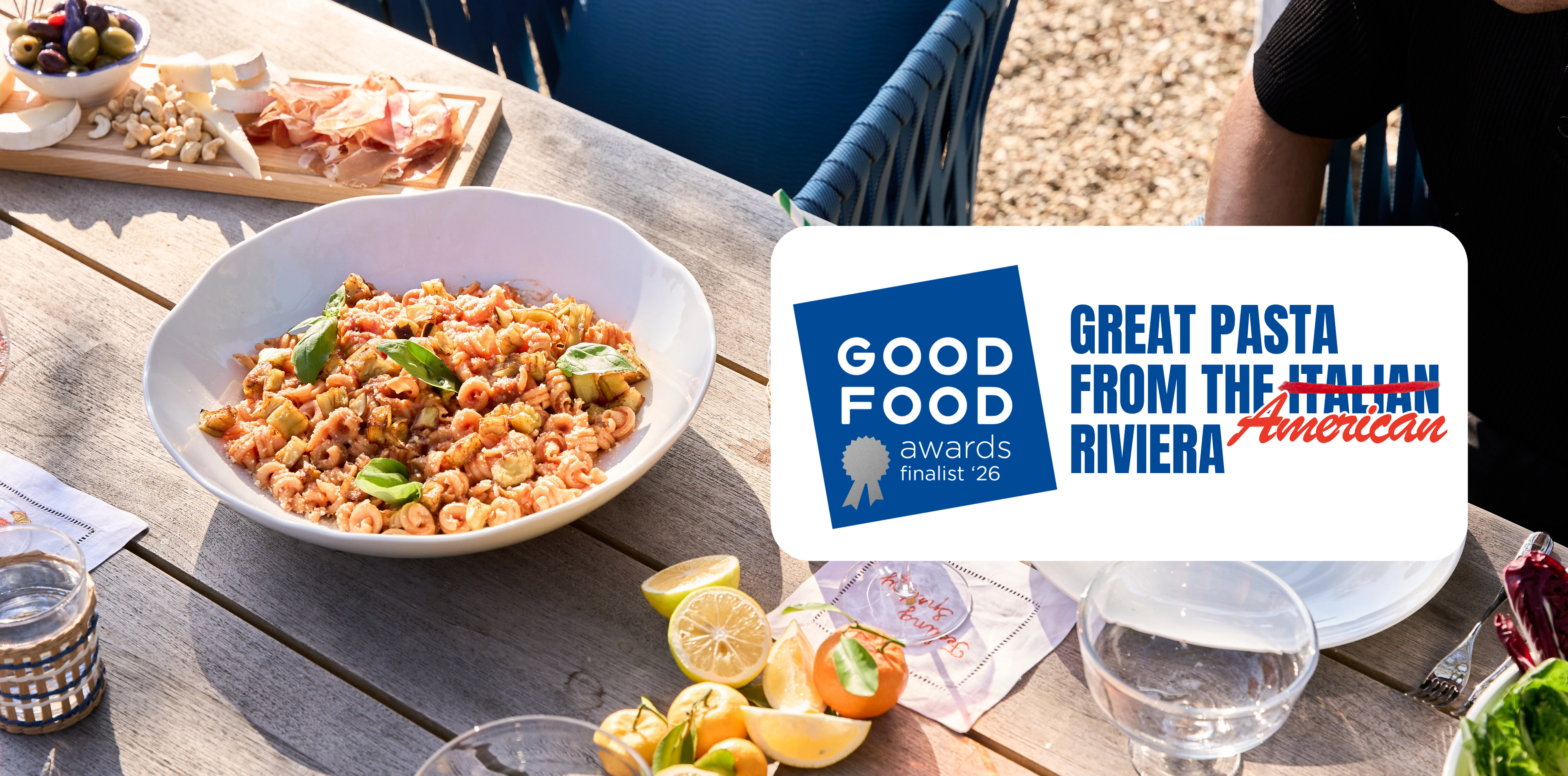 Pasta dish on a table with 'Good Food Awards' sign and 'Great Pasta from the American Riviera' text.