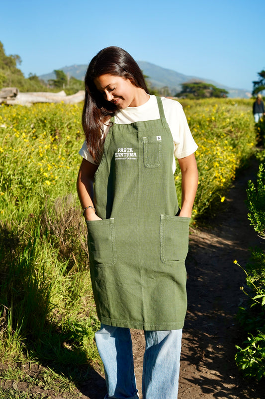 photo of model wearing green crossback apron hands in pockets
